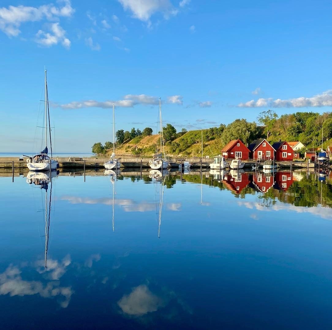 Ett somrigt Bäckviken med segelbåtar och fiskehoddor, blå himmel och hav.